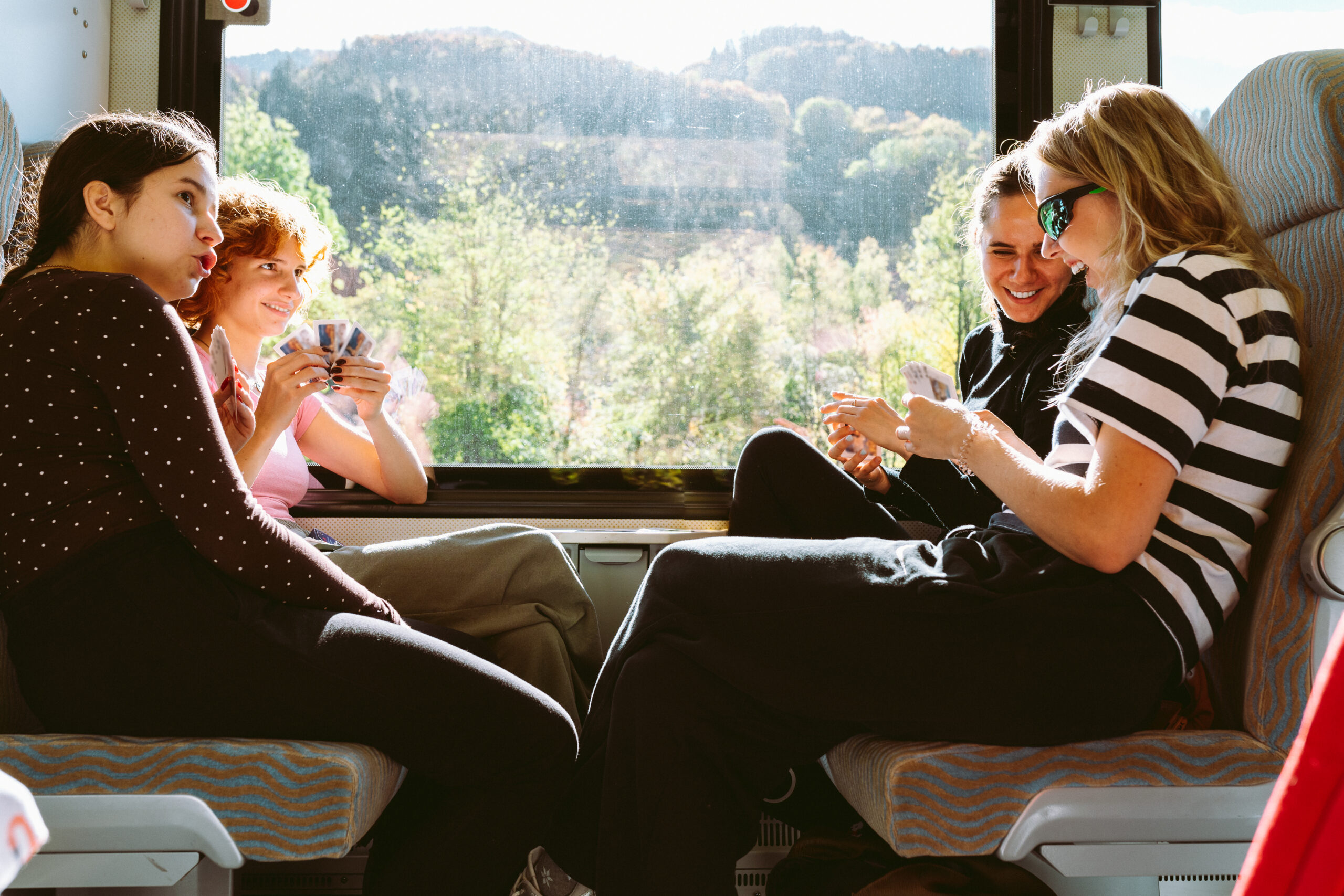 Cuatro amigas sonriendo y jugando a las cartas en los asientos de un tren